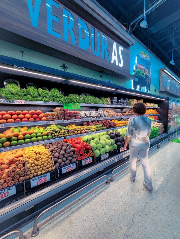 Woman browsing fresh fruits and vegetables in a supermarket aisle.